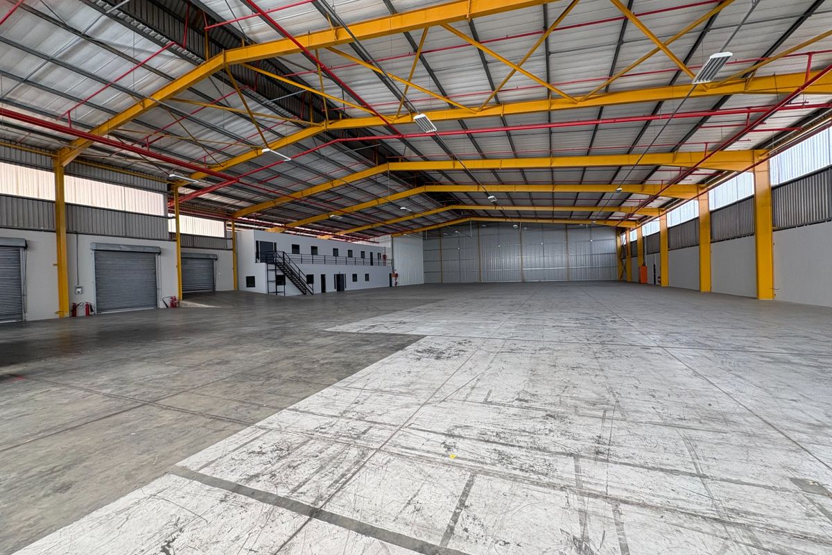 Expansive industrial warehouse space featuring high ceilings, steel portal frame construction, roller shutter access, and an integrated mezzanine office level.