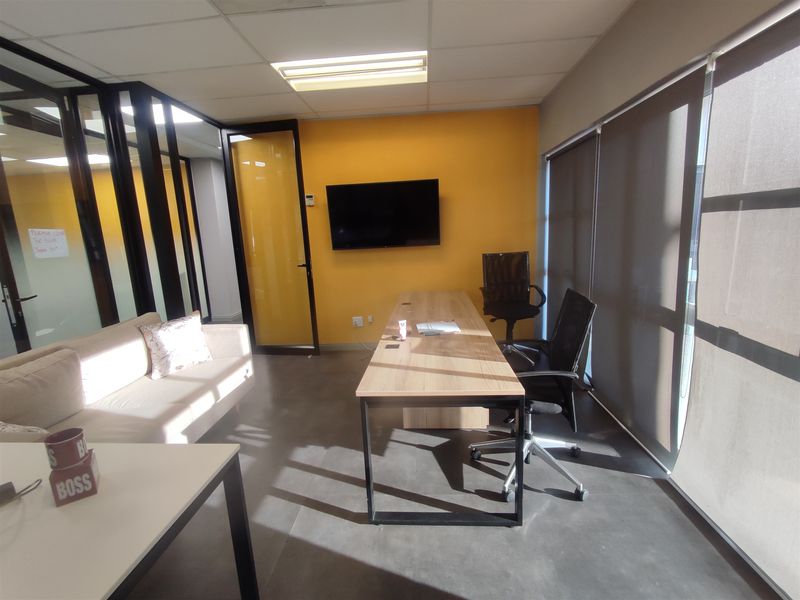 A modern office space featuring polished concrete floors, glass partition walls, and large windows with roller blinds, providing a professional and bright work environment.