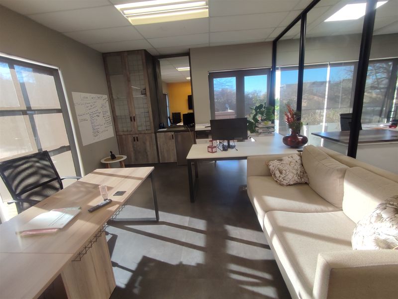 A modern office space featuring glass partitions, built-in cabinetry, suspended ceilings with recessed lighting, and large windows providing ample natural light.