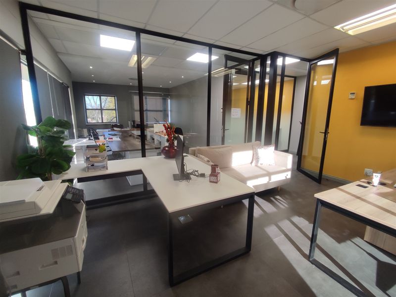 Modern office space featuring glass partition walls, black metal framing, tiled flooring, and recessed ceiling lighting, creating a professional and open work environment.