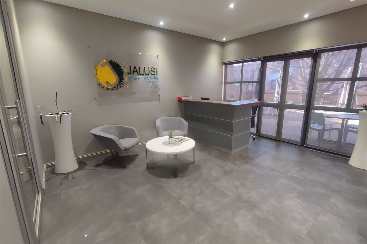 A professional office reception area featuring modern tiled flooring, recessed lighting, and a built-in reception desk with access to an outdoor patio.
