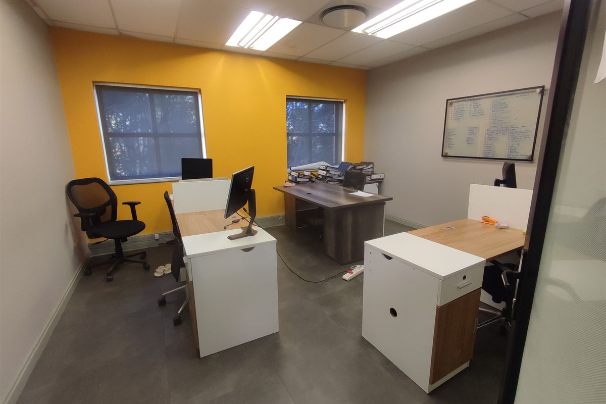 A functional office space featuring tiled flooring, recessed lighting, and large windows with roller blinds, providing a bright and professional work environment.