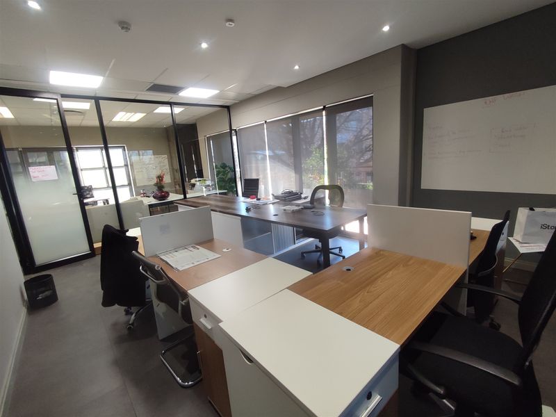 Modern office space featuring glass partitions, recessed lighting, and large windows with roller blinds, providing a professional and well-lit work environment.