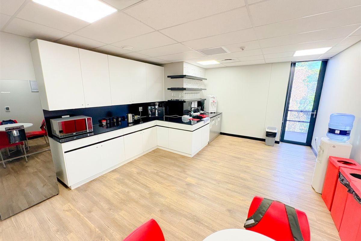 Modern office kitchenette featuring white cabinetry, black countertops, wood-look laminate flooring, and a glass door providing natural light.