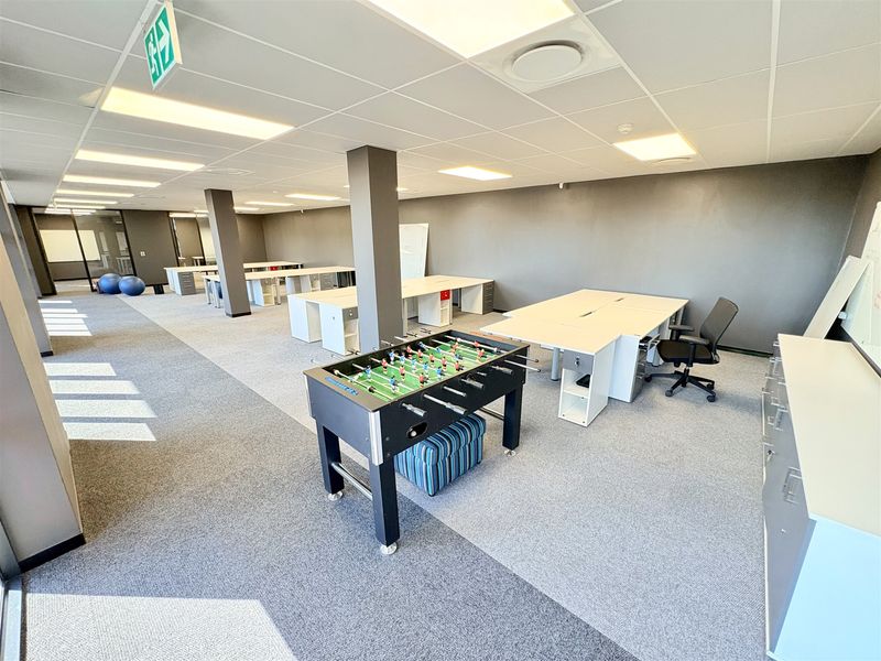Spacious open-plan office area featuring suspended ceilings, recessed lighting, carpeted flooring, and structural columns, providing a functional workspace environment.