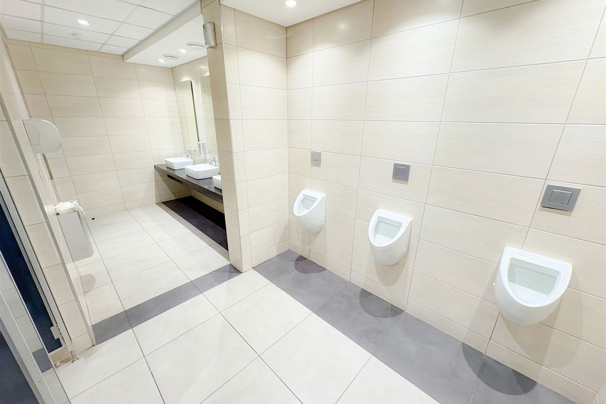 Modern commercial bathroom featuring wall-mounted urinals, sleek countertop washbasins, and neutral tiled finishes in excellent condition.