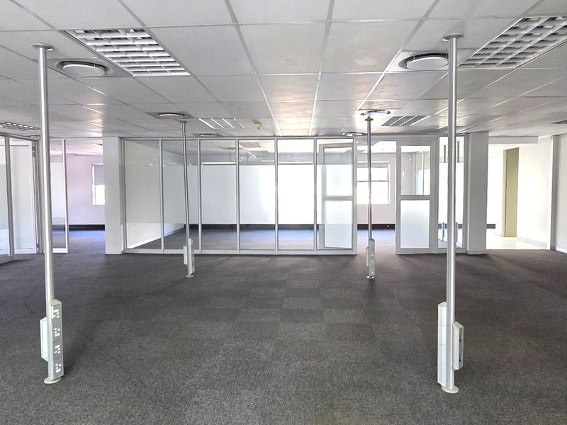 Spacious open-plan office area featuring glass partitions, suspended ceilings with recessed lighting, and carpeted flooring, providing a versatile and professional workspace.