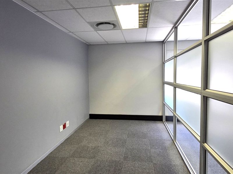A clean, empty office space featuring carpet tiles, a suspended ceiling with recessed lighting, and a modern frosted glass partition wall.