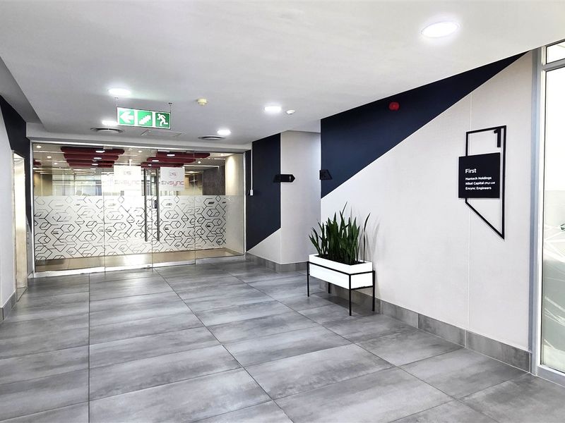A modern, well-maintained office building entrance lobby featuring tiled floors, recessed lighting, and glass entry doors with clear directional signage.