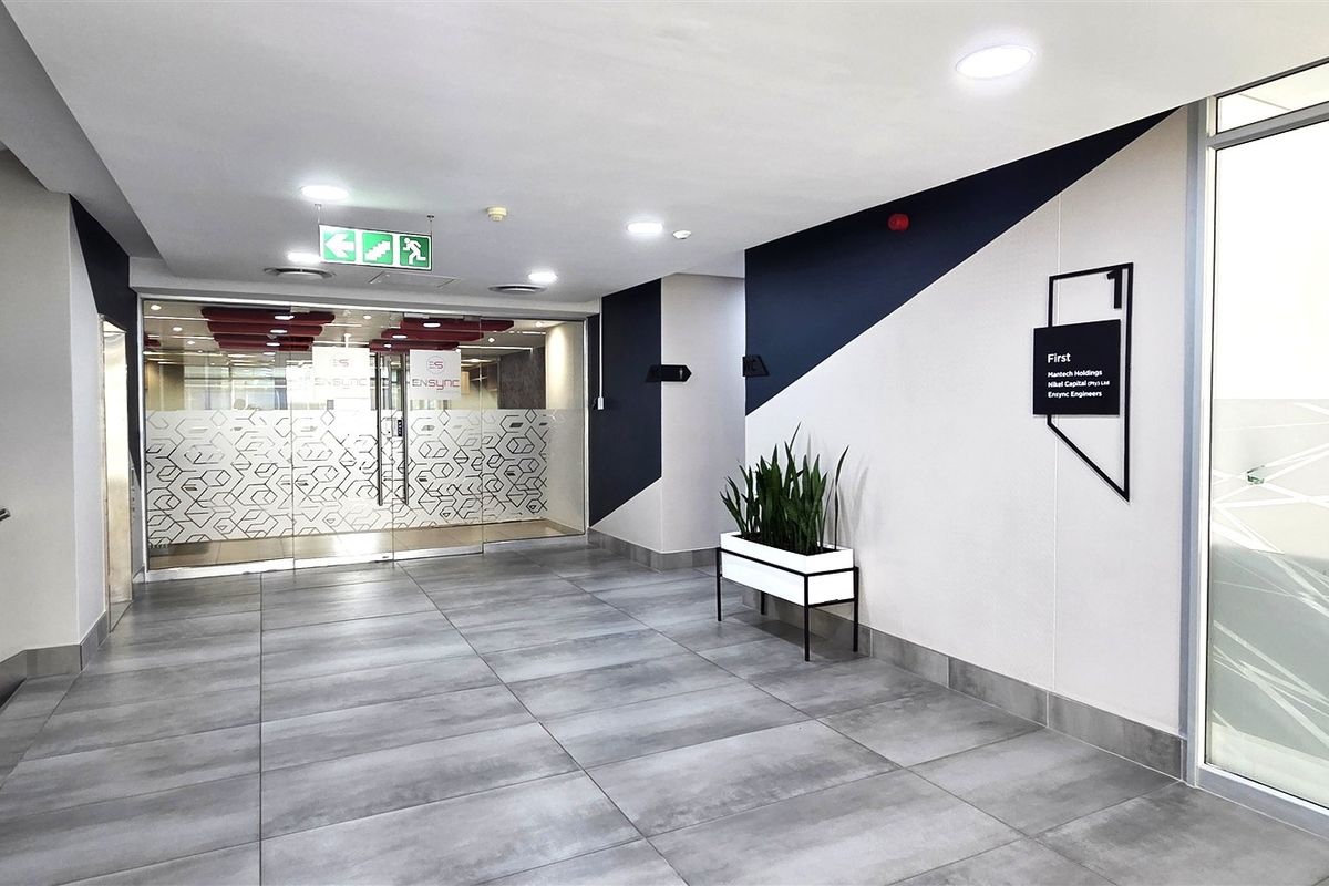 A modern, well-maintained office building entrance lobby featuring tiled floors, recessed lighting, and glass entry doors with clear directional signage.