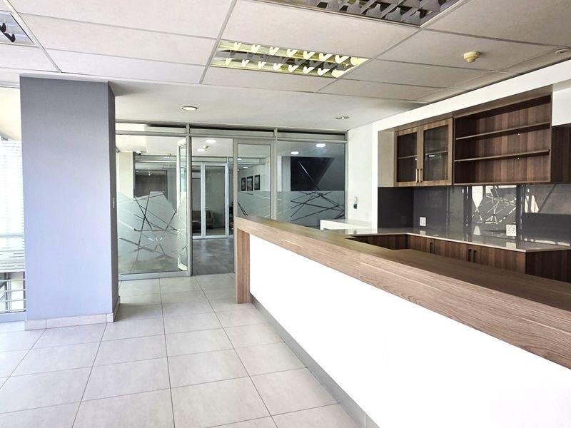 Modern office space featuring a built-in reception counter, glass partitions, tiled flooring, and integrated cabinetry with recessed ceiling lighting.
