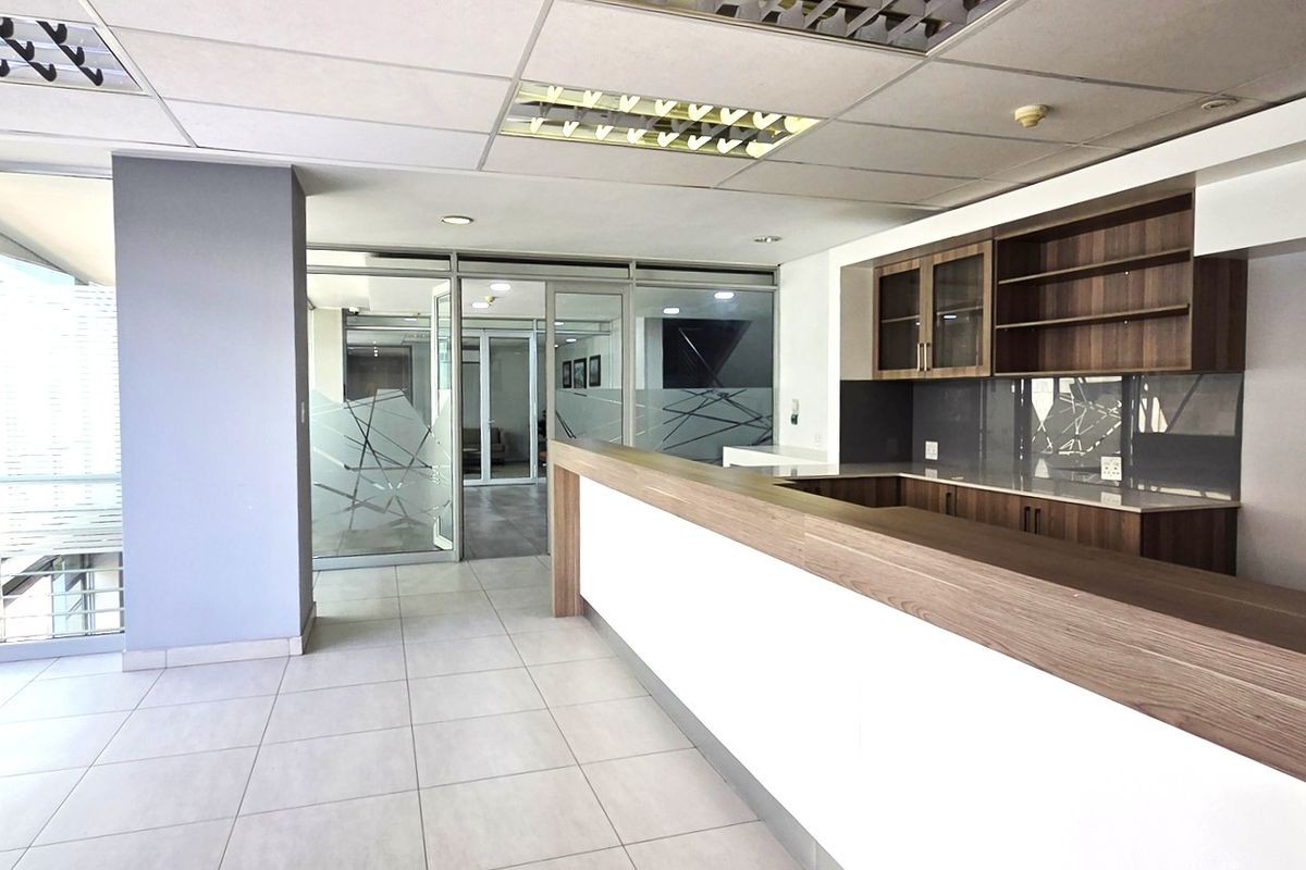 Modern office space featuring a built-in reception counter, glass partitions, tiled flooring, and integrated cabinetry with recessed ceiling lighting.
