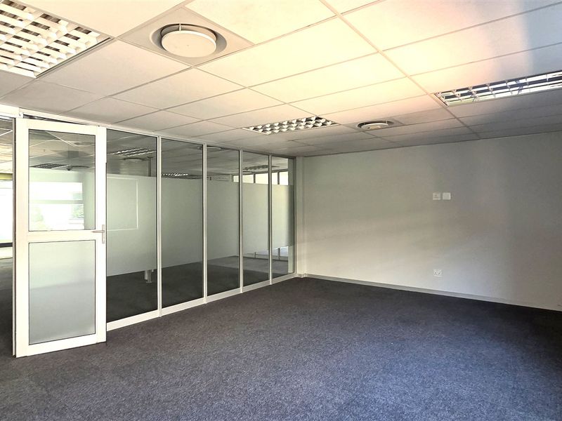 A bright, vacant office space featuring glass partition walls, suspended ceilings with recessed lighting, and neutral carpeting, ideal for a professional workspace.