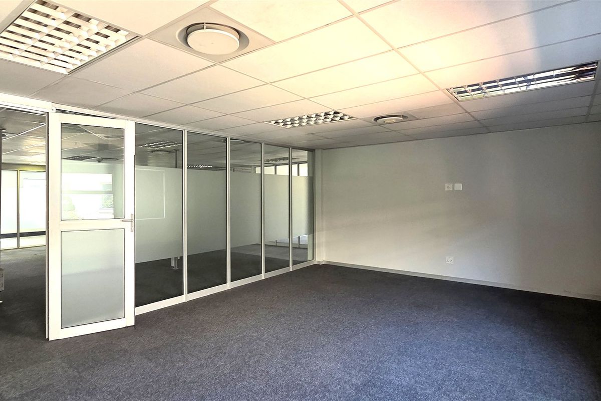 A bright, vacant office space featuring glass partition walls, suspended ceilings with recessed lighting, and neutral carpeting, ideal for a professional workspace.
