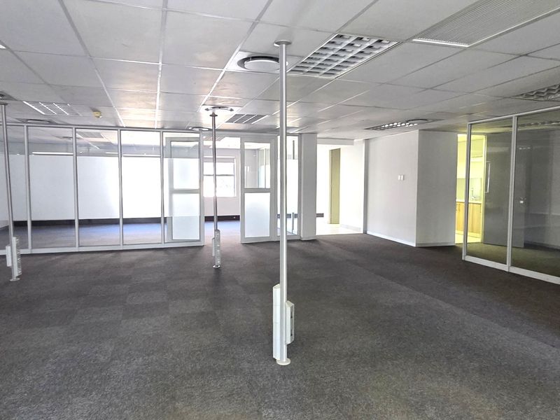 Spacious open-plan office area featuring glass partition walls, suspended ceilings with recessed lighting, and carpeted flooring.