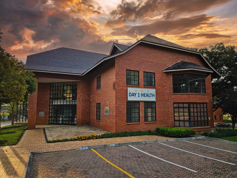 A professional exterior view of a well-maintained brick office building featuring a paved parking area and landscaped garden beds at sunset.