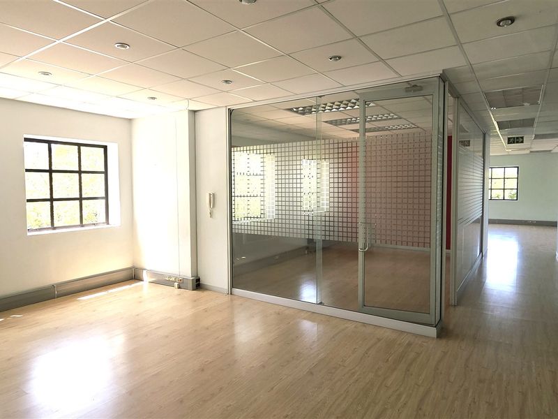 A bright, open-plan office space featuring laminate flooring, a suspended ceiling, and a modern glass partition wall creating a private meeting area.