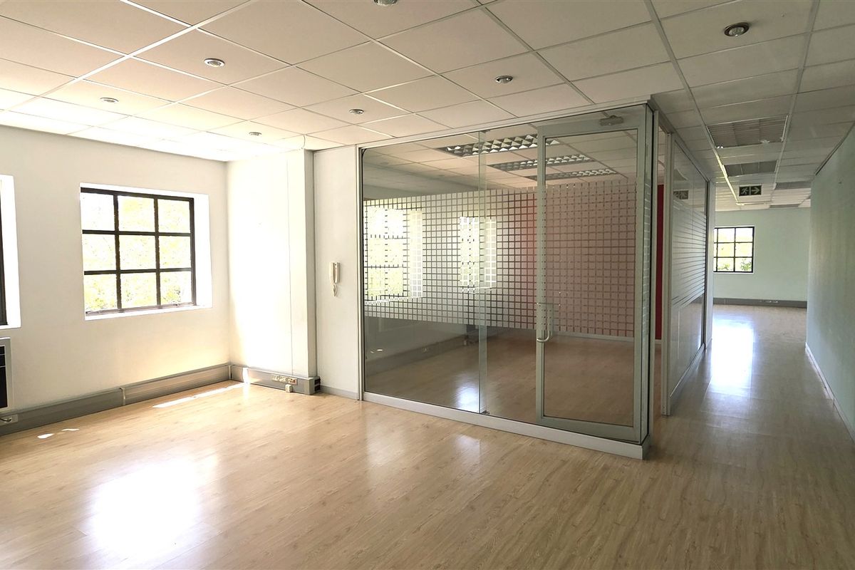 A bright, open-plan office space featuring laminate flooring, a suspended ceiling, and a modern glass partition wall creating a private meeting area.