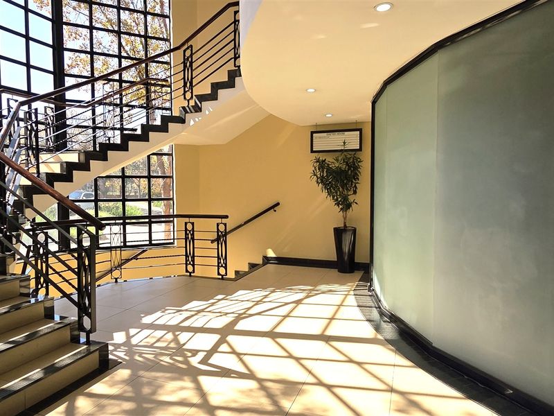 A bright and modern office entrance lobby featuring a prominent staircase, large glass curtain wall, and a curved frosted glass partition.