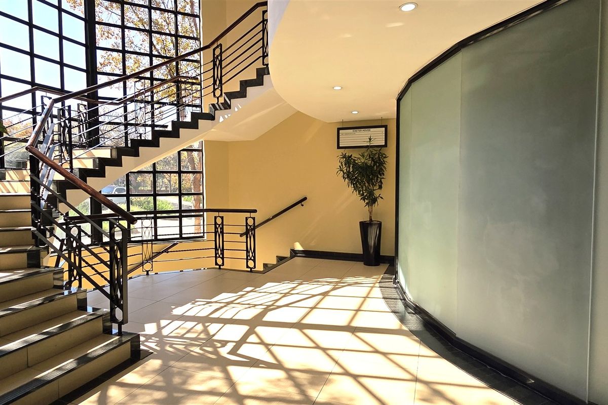 A bright and modern office entrance lobby featuring a prominent staircase, large glass curtain wall, and a curved frosted glass partition.