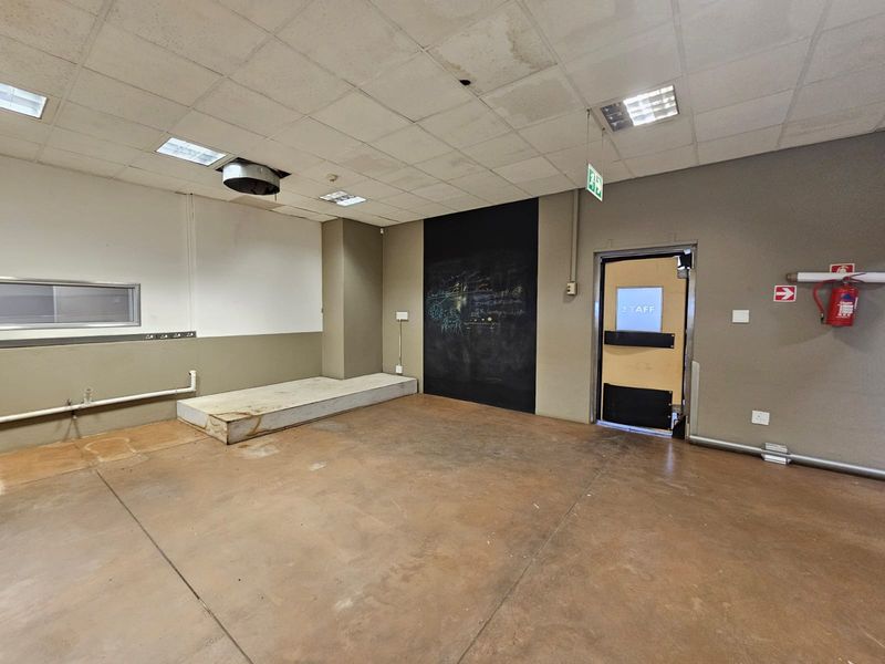 An empty utility or back-of-house space featuring a raised platform, suspended ceiling, and staff access door, suitable for storage or operational use.