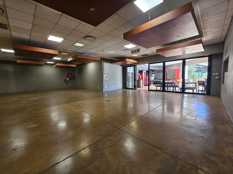 Spacious open-plan retail or commercial area featuring polished concrete floors, suspended ceiling tiles, and large sliding glass doors providing natural light and outdoor access.