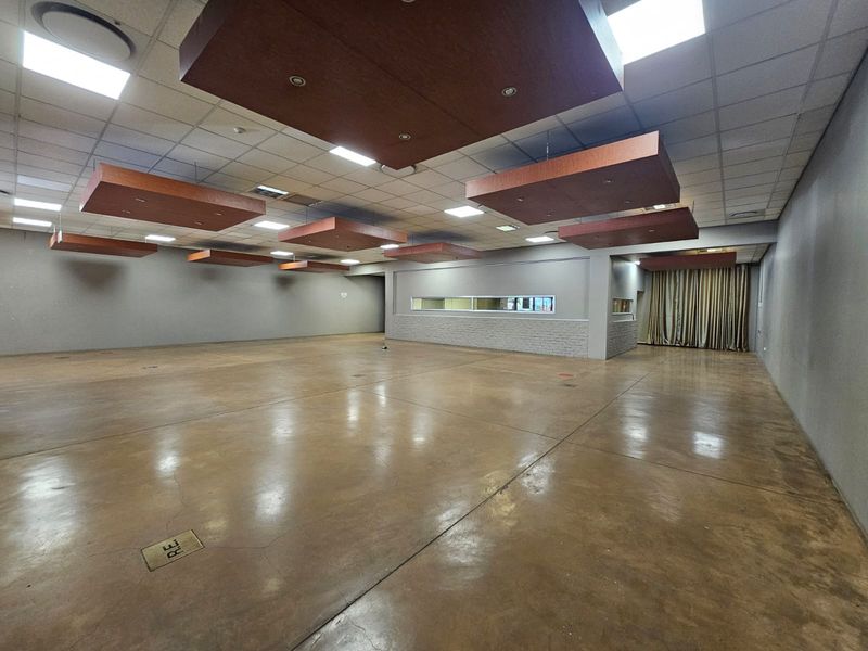 A spacious, open-plan retail or commercial area featuring polished concrete floors, a suspended ceiling with decorative acoustic panels, and integrated floor power points.