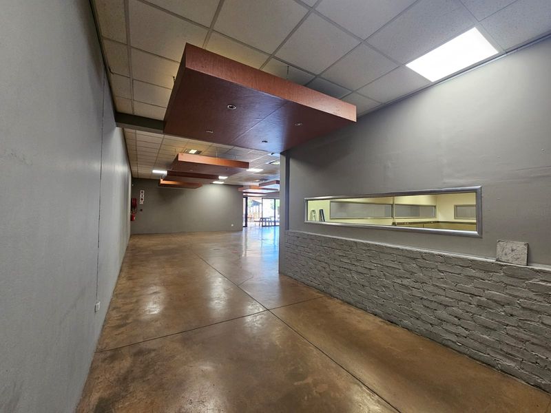 Spacious open-plan retail area featuring polished concrete floors, a suspended ceiling with decorative bulkheads, and a brick feature wall with an internal viewing window.