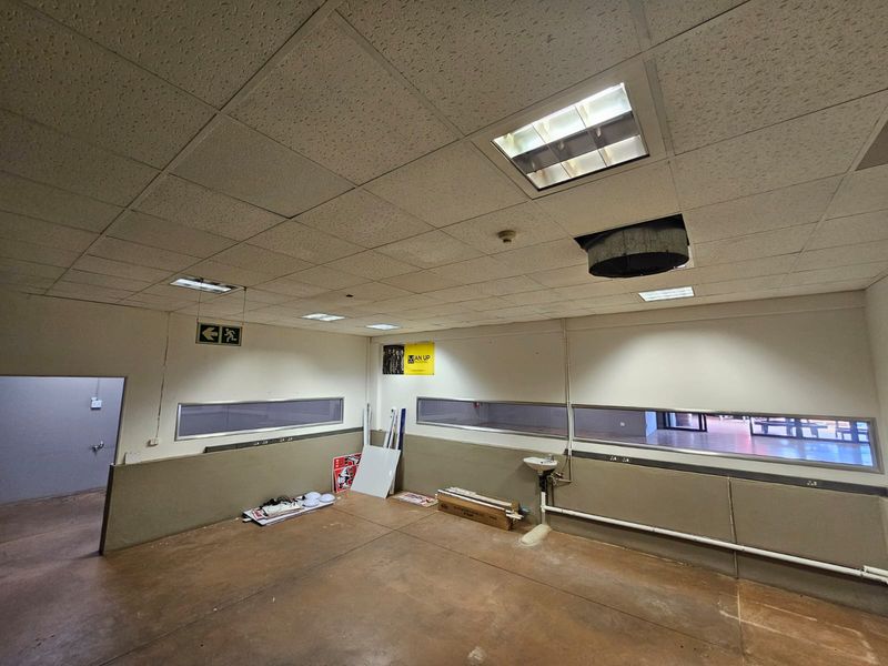 An open-plan utility or office space featuring a suspended ceiling, horizontal windows, and a wall-mounted basin, currently in need of maintenance and refurbishment.