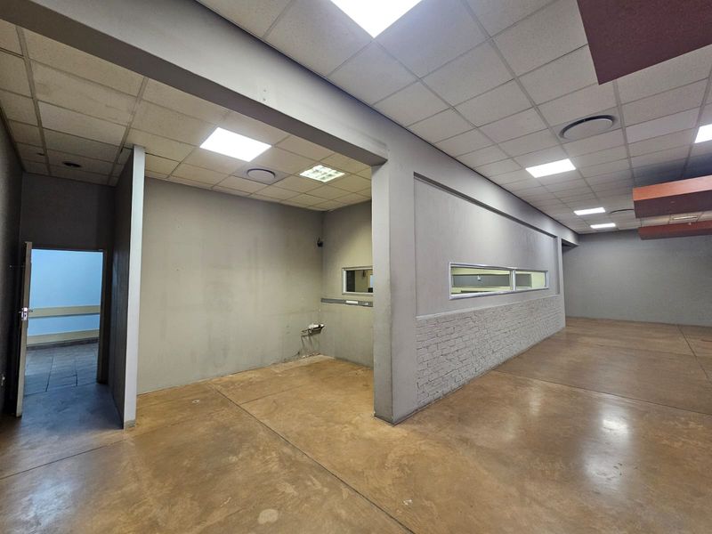 Spacious open-plan retail area featuring polished concrete floors, suspended ceilings with recessed lighting, and a textured brick feature wall.