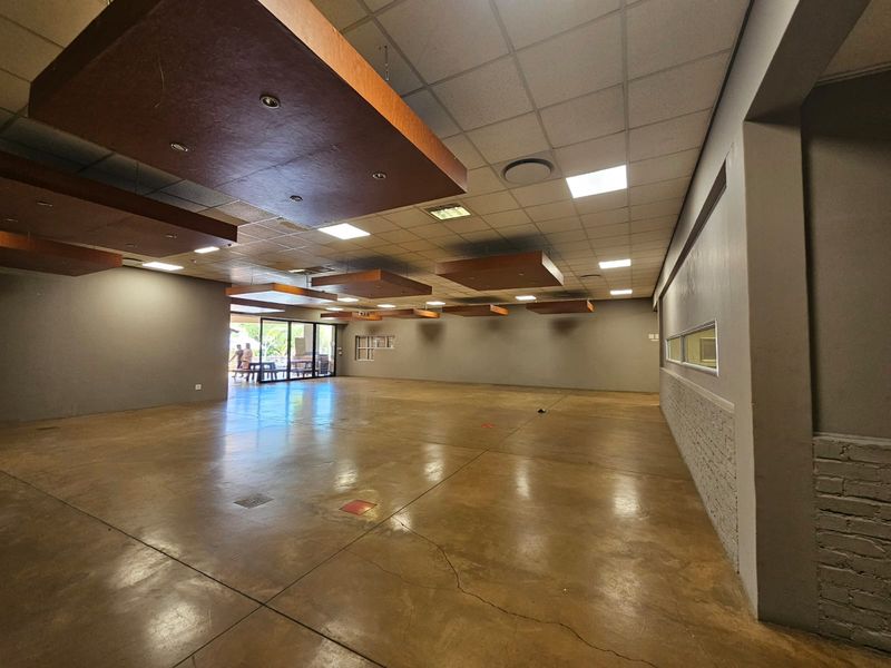 Spacious open-plan retail or commercial area featuring polished concrete floors, suspended ceiling tiles with decorative wooden bulkheads, and large sliding glass doors.