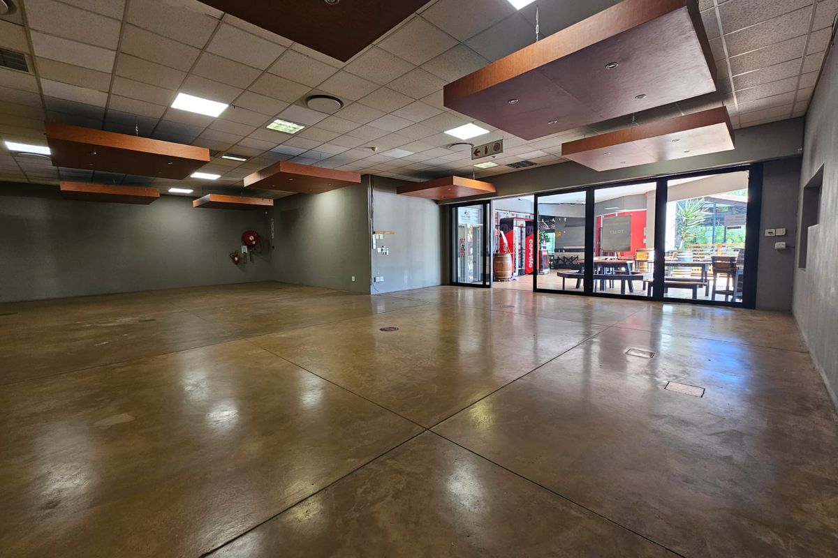 Spacious open-plan retail or commercial area featuring polished concrete floors, suspended ceiling tiles, and large sliding glass doors providing natural light and outdoor access.