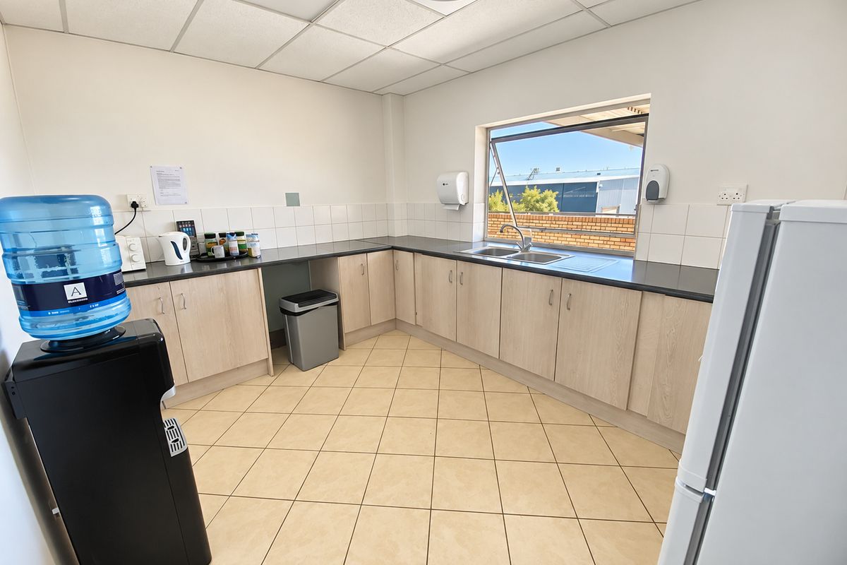 Functional industrial kitchen area featuring light wood-tone cabinetry, dark countertops, a stainless steel double sink, and durable tiled flooring.