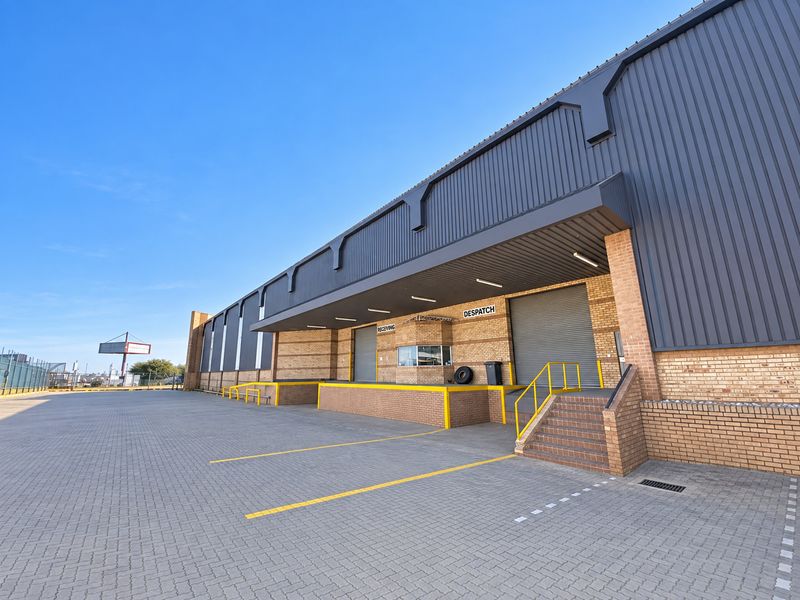 Industrial warehouse exterior featuring a paved loading yard, multiple roller shutter doors for receiving and dispatch, and a dedicated security office.