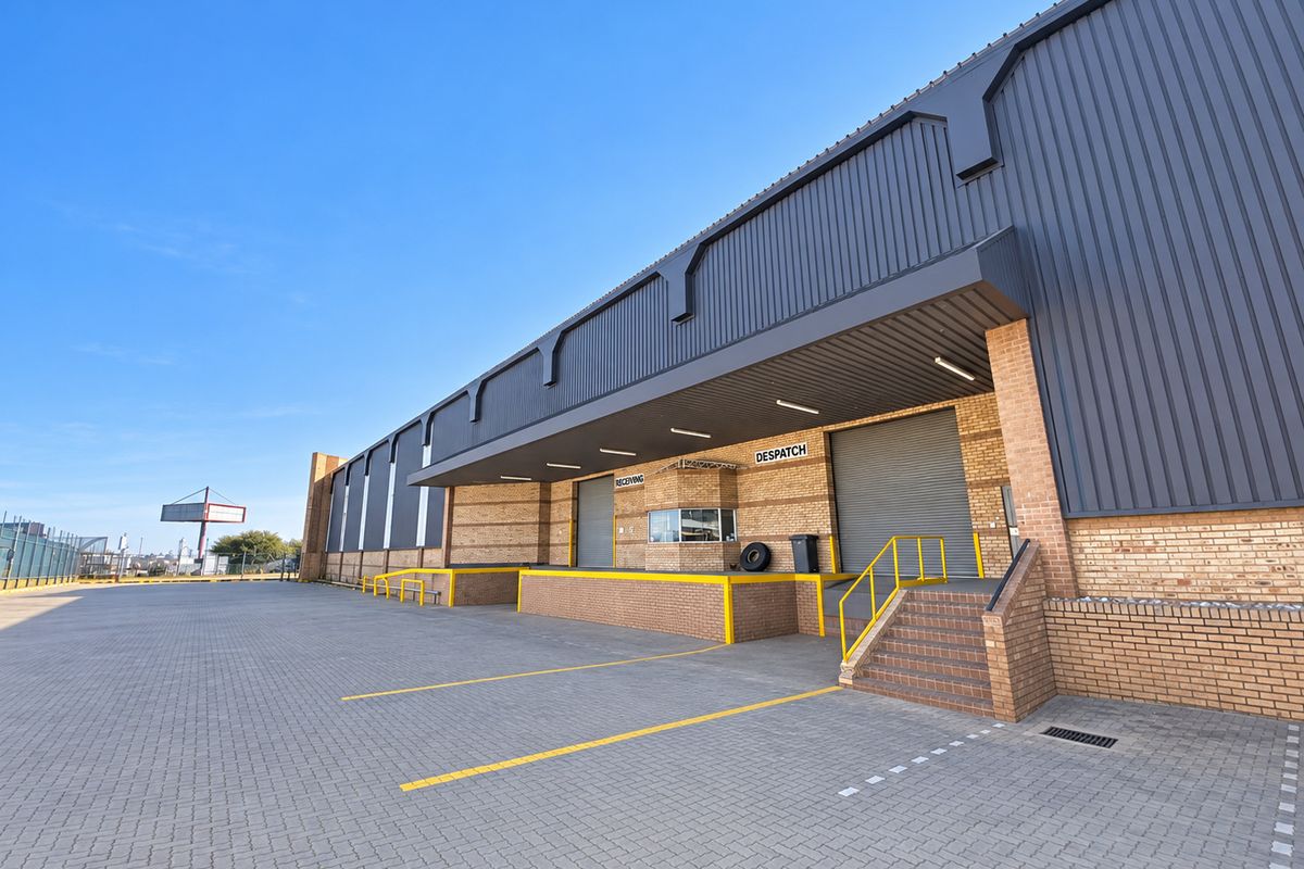 Industrial warehouse exterior featuring a paved loading yard, multiple roller shutter doors for receiving and dispatch, and a dedicated security office.