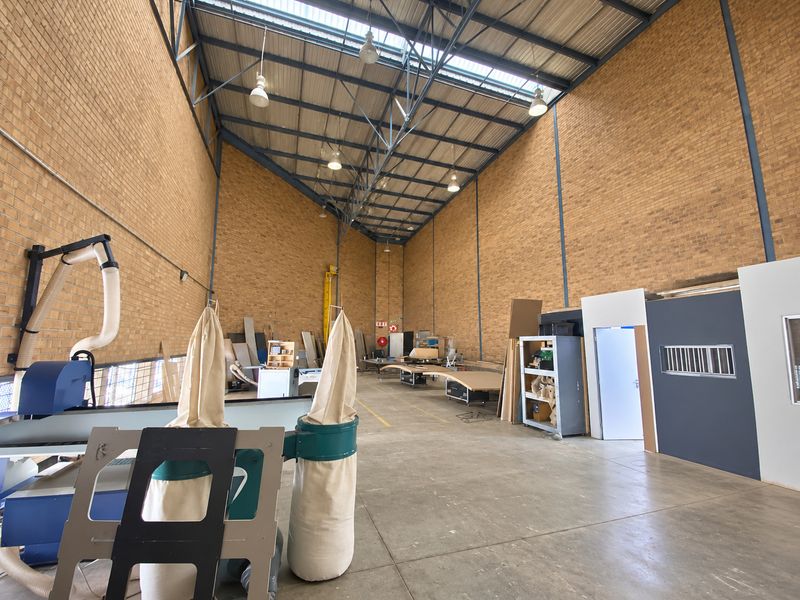 Spacious industrial workshop featuring high ceilings with exposed steel trusses, face brick walls, durable concrete flooring, and integrated dust extraction infrastructure.