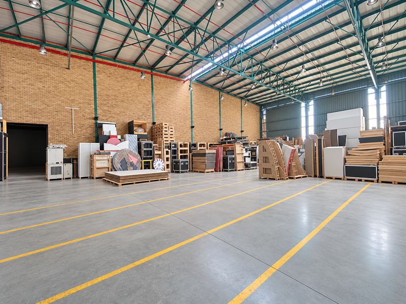 Spacious industrial warehouse featuring high-clearance exposed steel truss roofing, polished concrete flooring with safety markings, and durable brick wall construction.