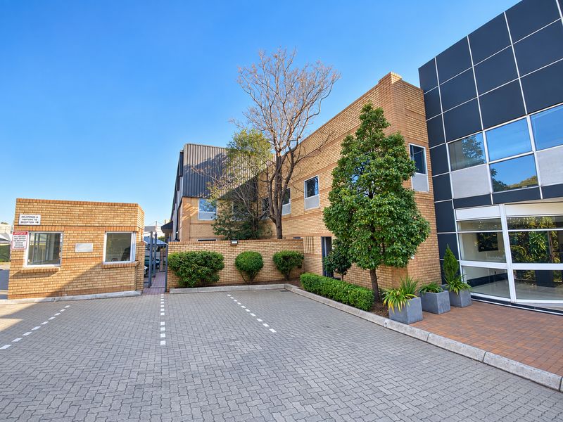 Front exterior view of an industrial property featuring a paved parking area, brick facade, and a dedicated security gatehouse entrance.