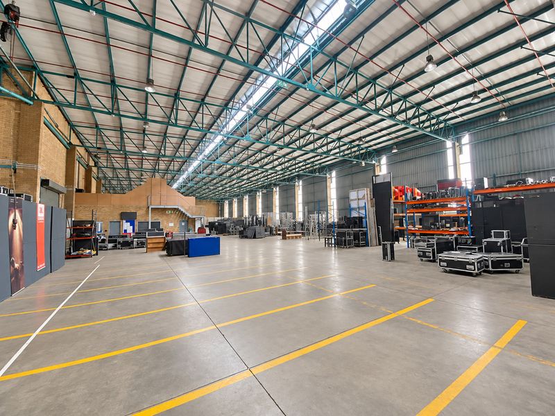 Spacious industrial warehouse featuring high ceilings with exposed steel trusses, concrete flooring, and ample natural light through integrated skylights.