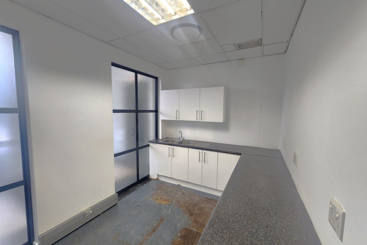 A small office kitchenette featuring built-in cabinetry, laminate countertops, a stainless steel sink, and a drop ceiling with integrated lighting.