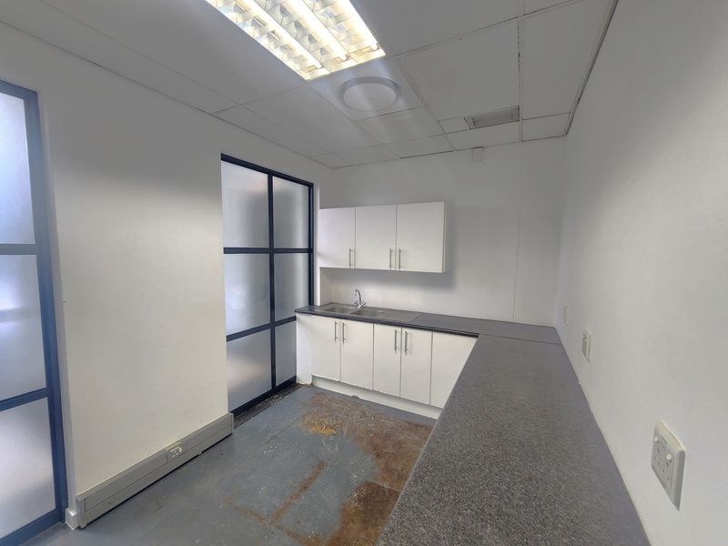 A small office kitchenette featuring built-in cabinetry, laminate countertops, a stainless steel sink, and a drop ceiling with integrated lighting.