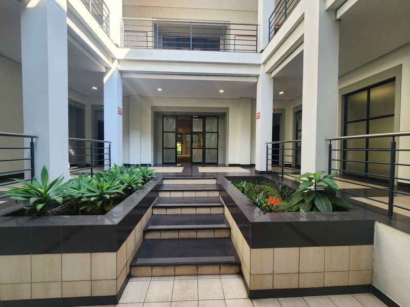 A well-maintained office building courtyard featuring a central tiled staircase, built-in planters, and modern glass entrance doors.