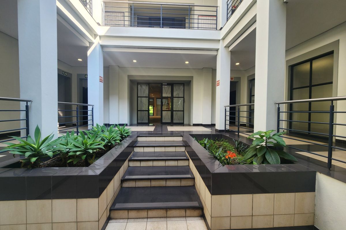 A well-maintained office building courtyard featuring a central tiled staircase, built-in planters, and modern glass entrance doors.