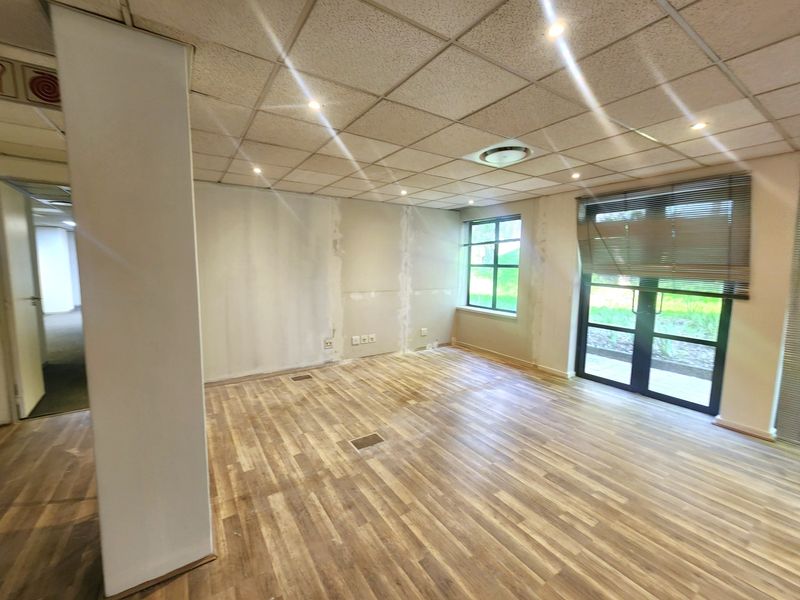 An empty office space featuring a suspended ceiling, recessed lighting, laminate flooring, and glass doors leading to an outdoor area.
