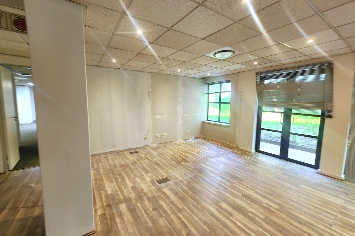 An empty office space featuring a suspended ceiling, recessed lighting, laminate flooring, and glass doors leading to an outdoor area.