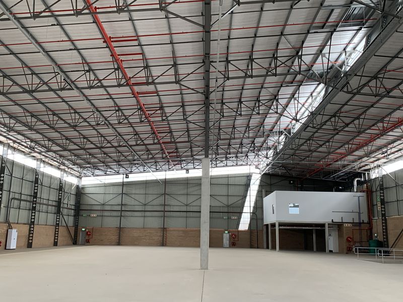 Spacious industrial warehouse featuring high ceilings with exposed steel trusses, fire sprinkler systems, concrete flooring, and a mezzanine level.