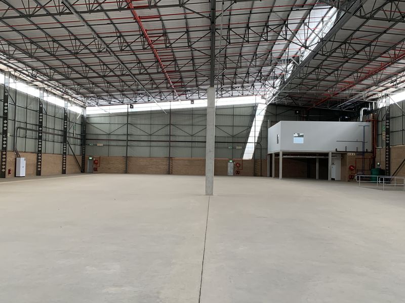 Spacious industrial warehouse featuring high ceilings with exposed steel trusses, concrete flooring, fire sprinkler system, and a mezzanine level for versatile storage or office use.