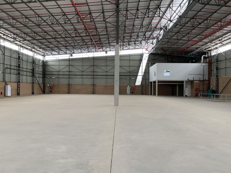 Spacious industrial warehouse featuring high ceilings with exposed steel trusses, concrete flooring, fire sprinkler system, and an integrated mezzanine level.