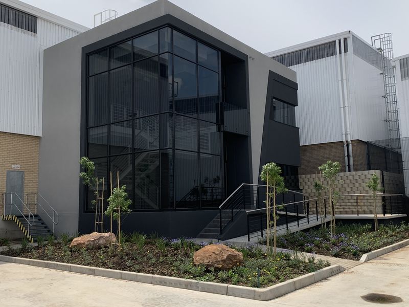 Modern industrial office facade featuring a striking glass curtain wall, contemporary metal cladding, and a landscaped entrance with a concrete accessibility ramp.