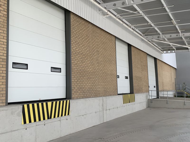 Industrial loading bay area featuring multiple roller shutter doors, a concrete loading dock with safety bumpers, and a protective metal canopy.